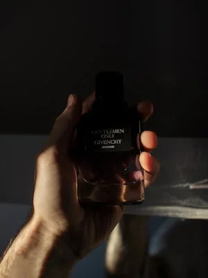 A man's hand holds a Givenchy perfume bottle with dramatic lighting.