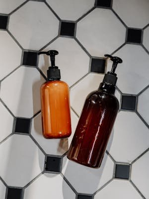 Minimalist flatlay of reusable cosmetic bottles on geometric tile floor promoting zero waste lifestyle.