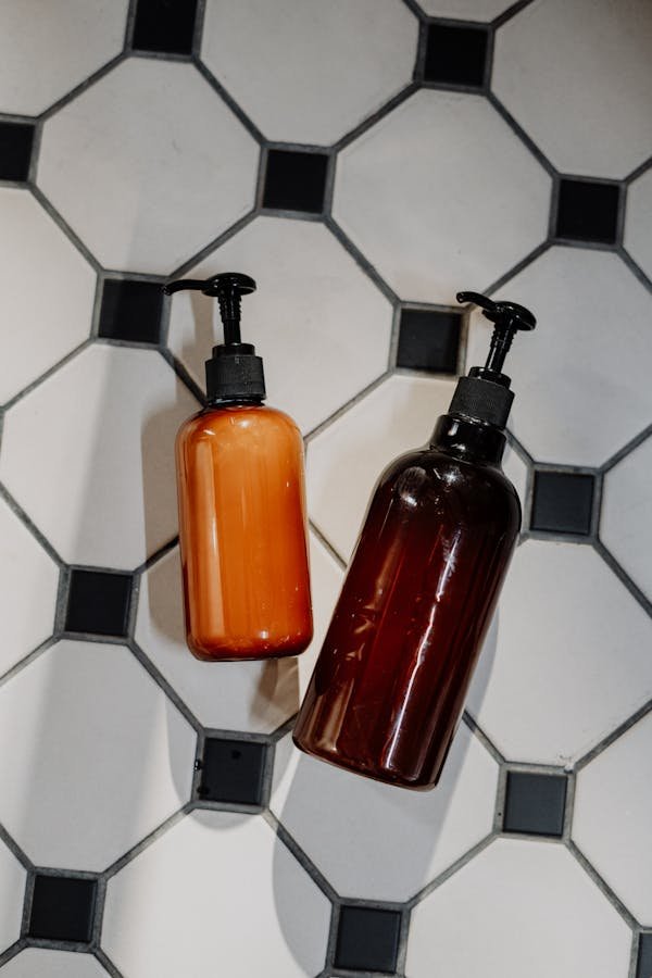 Minimalist flatlay of reusable cosmetic bottles on geometric tile floor promoting zero waste lifestyle.